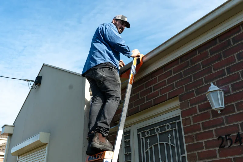 Roof plumber on a ladder checking gutters and downpipes in Altona